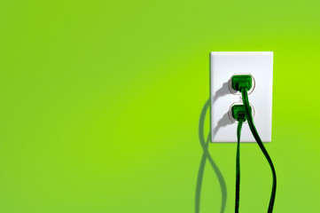 Green power cords in eletric outlet on a green colored wall