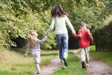 Naklejka na ściany i meble Mother and children running along woodland path