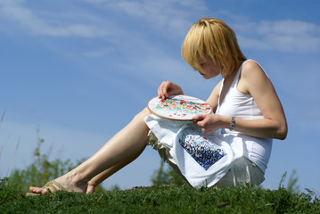 woman cross-stitching in the park with blue sky on background