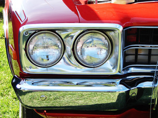 Head lights and chrome bumper of a bright red muscle car