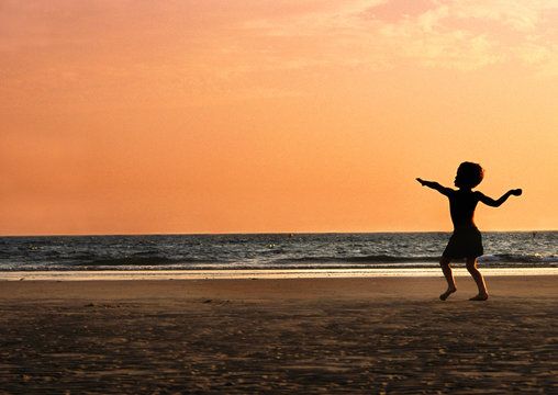 Boy Throwing Sand On Beach At Sunset