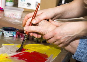a nurse holds the hands of a senior citizen and helps her paint with a brush