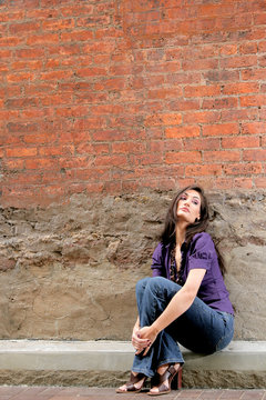 woman sitting against a brick wall