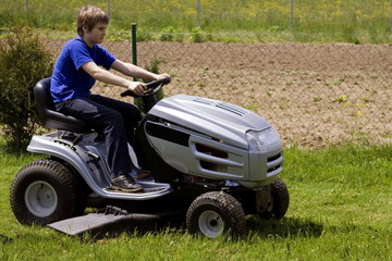 Teen boy cutting lawn with small tractor.