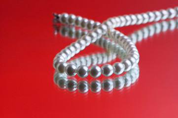 Pearl necklace on the red reflective background
