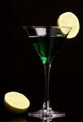Green cocktail with green lemon on black background