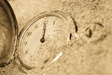 Vintage pocket clock buried in sand. Lost time concept.