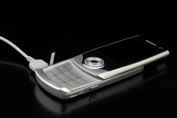 Silver cell phone conected to charger - on shiny black 