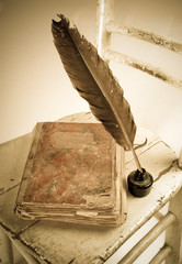 Old book, quill and bottle of black ink on old wooden chair