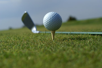 Golf ball in tall green grass set against blue sky