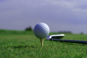 Golf ball in tall green grass set against blue sky