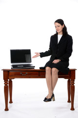 Business woman sitting on a desk with an open laptop.