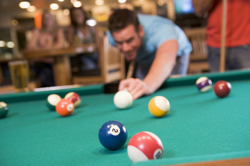 Young man playing pool in a bar (focus on pool table)