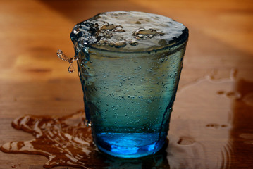 bicchiere azzurro colmo di acqua con schizzi su tavolo di legno