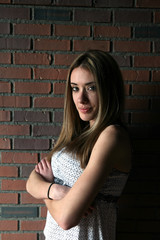 Fototapeta na wymiar Pretty teenage girl with arms crossed; against a brick wall