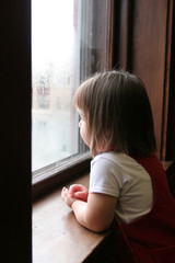 Little girl looking out the window at a rainy day outside.