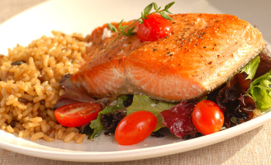 Piece of seared salmon on a bed of greens with tomatoes and brow