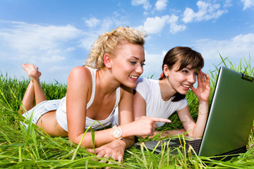 Two beautiful girls are laughing near laptop outdoors