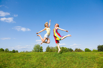 Two happy girls jumping together on green meadow