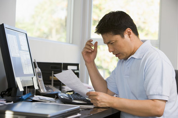 Man in home office with computer and paperwork frustrated