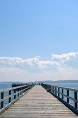 Fototapeta na wymiar Wooden pier extending into ocean, under hazy blue sky and clouds