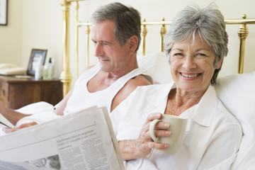 Couple in bedroom with coffee and newspapers smiling