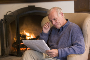 Man sitting in living room by fireplace with newspaper