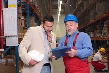 boss and older worker talking over papers in warhouse