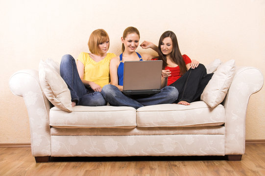 three girls sitting on a lounge with a laptop