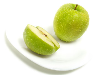 Half and whole green apple on plate