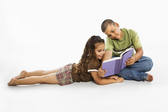 Hispanic Boy And Girl Reading Book Together.