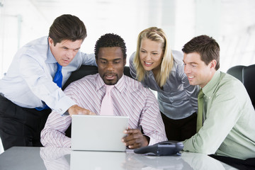 Four businesspeople in a boardroom at laptop smiling