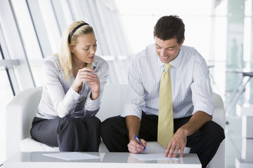 Two businesspeople sitting in office lobby talking and smiling