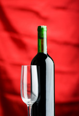 Wine glass and bottle against red background