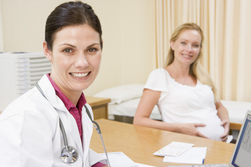 Doctor with laptop and pregnant woman in doctor's office smiling