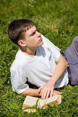 Naklejka na ściany i meble A young man reads a book, lying on a grass.