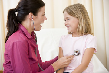 Doctor giving checkup with stethoscope to young girl in exam roo