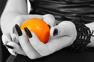 Fototapeta premium Colored mandarine in black-white hands of a gothic girl