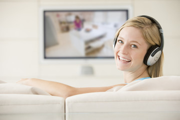 Woman in living room watching television and wearing headphones