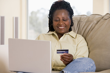 Woman in living room using laptop holding credit card and smilin