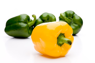 Gelber Paprika vor drei grünen Schoten