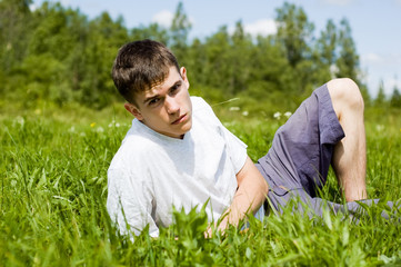 Naklejka na ściany i meble A young man reads a book, lying on a grass.