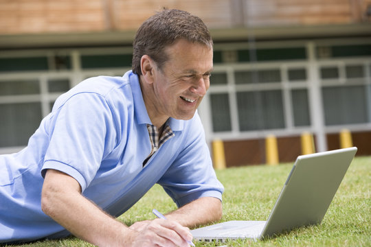 Man using laptop while lying in grass on campus