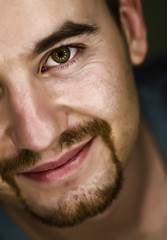  close-up portrait of a Caucasian man with beard, looking into the camera and smile. safe and calm expression, reflections of circular lights in the eyes.