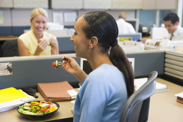 Businesswoman in cubicle eating salad
