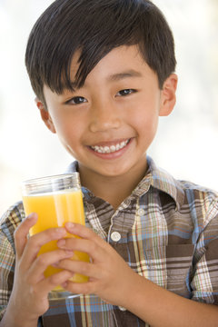 Young boy indoors drinking orange juice smiling