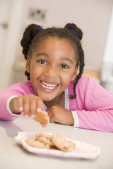 Young girl in kitchen eating cookies smiling