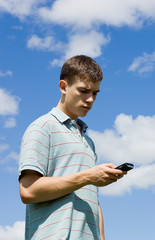 A young man speaks by phone on a background sky.