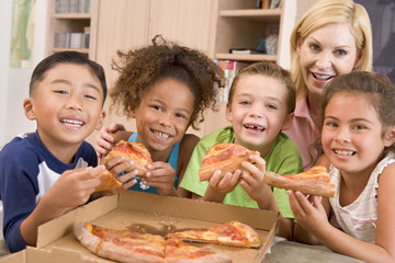 Four young children with woman eating pizza smiling