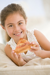 Young girl eating pizza slice in living room smiling